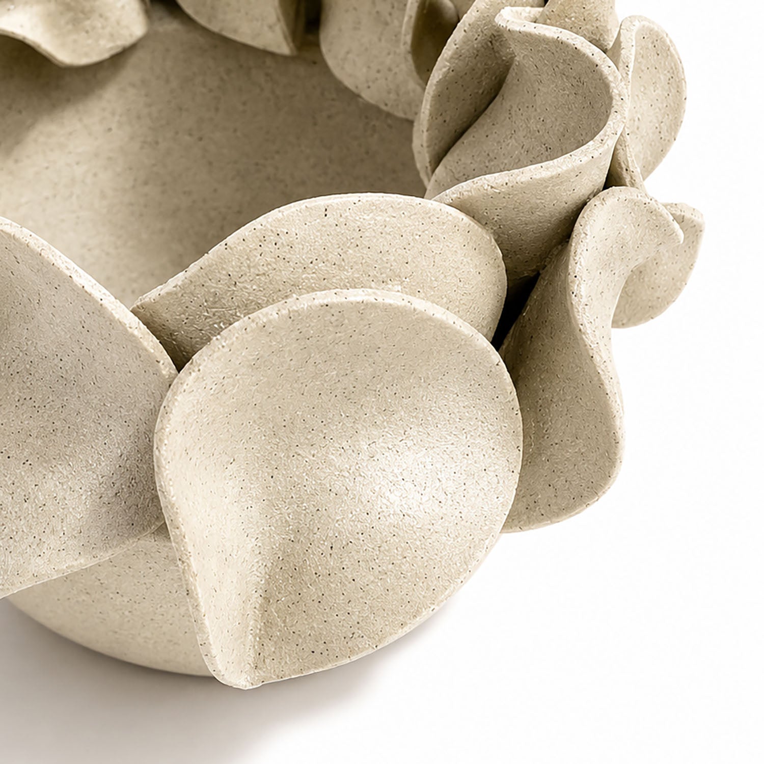 A close-up of a sculptural ceramic planter with layered, ruffled petal-like edges and a speckled light beige finish.