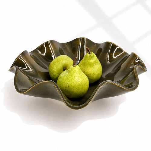 An oily Rockpool coloured wavy ceramic bowl with a glossy glaze, containing three green pears, set against a clean white background with soft window shadow patterns.